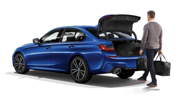BMW 3 serijos sedanas, automatinis bagažinės atidarymas Stovinčio BMW 3 serijos sedano trijų ketvirčių vaizdas iš galo, vairuotojui automatiškai koja atidarant bagažinės dangtį.