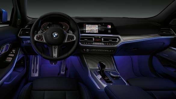 BMW 3 serijos sedanas, aplinkos apšvietimas. BMW 3 serijos sedano vairuotojo erdvės su mėlynu Ambient apšvietimu kojų nišoje vaizdas iš priekio.