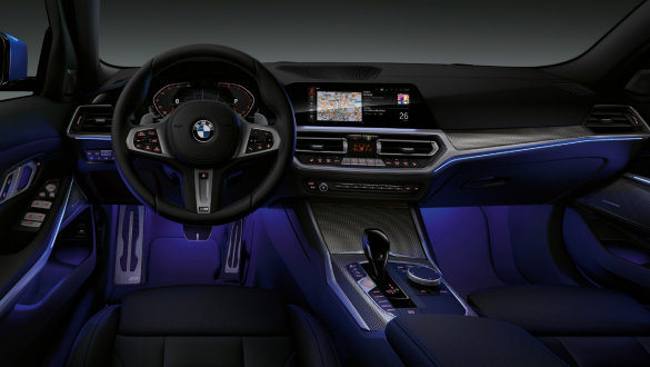 BMW 3 serijos sedanas, aplinkos apšvietimas. BMW 3 serijos sedano vairuotojo erdvės su mėlynu Ambient apšvietimu kojų nišoje vaizdas iš priekio.