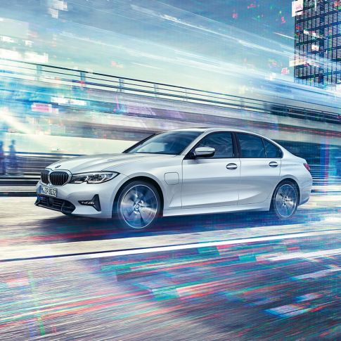 BMW 3 serijos sedano 330e, važiuojančio keliu, vaizdas iš šono. Keliu važiuojančio BMW 3 serijos sedano 330e vaizdas iš šono miesto fone.