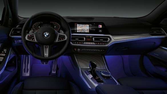 BMW 3 serijos sedano (G20) aplinkos apšvietimas BMW 3 serijos sedano (G20) vairuotojo erdvės vaizdas iš priekio su kojų zona, apšviesta mėlynu <i>Ambient</i> aplinkos apšvietimu.