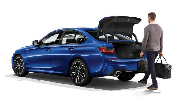 BMW 3 serijos sedanas (G20), automatinis bagažinės valdymas Stovinčio BMW 3 serijos sedano (G20) trijų ketvirčių vaizdas iš galo, vairuotojui automatiškai koja atidarant bagažinės dangtį.