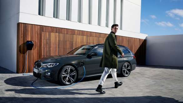 Įkraunamas hibridinis BMW 3 serijos Touring (G21) 2021, trijų ketvirčių vaizdas iš šono prie <i>Wallbox</i> stotelės Įkraunamas hibridinis BMW 3 serijos Touring (G21) 2021, trijų ketvirčių vaizdas iš šono prie <i>Wallbox</i> stotelės su modeliu