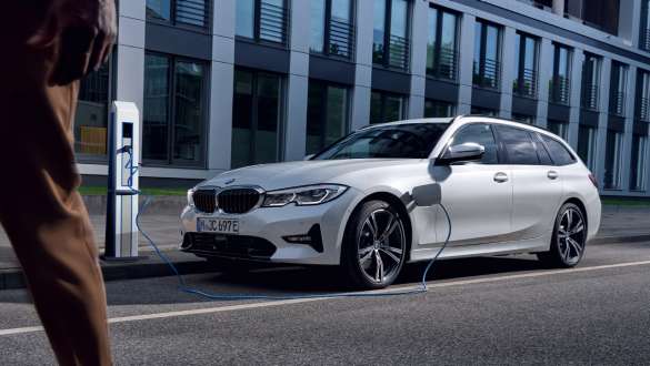 Įkraunamas hibridinis BMW 3 serijos Touring (G21) 2021, įkraunamo automobilio trijų ketvirčių vaizdas Įkraunamas hibridinis BMW 3 serijos Touring (G21) 2021, įkraunamo automobilio trijų ketvirčių vaizdas iš priekio pastato fone