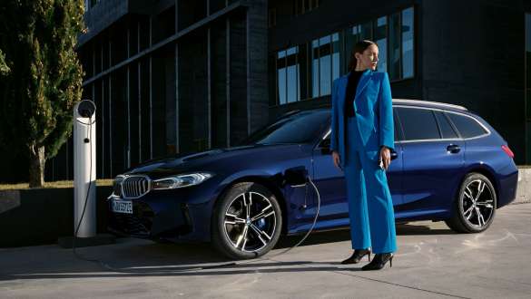 BMW 3 serijos įkraunamo hibridinio Touring G21 trijų ketvirčių vaizdas iš šono prie įkrovimo stotelės BMW 3 serijos įkraunamo hibridinio Touring G21 trijų ketvirčių vaizdas iš šono su modeliu prie įkrovimo stotelės