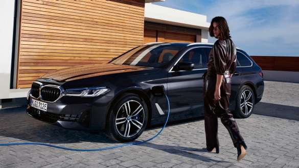 Įkraunamas hibridinis BMW 5 serijos Touring (G31) 2021 LCI, įkraunamo automobilio trijų ketvirčių vaizdas iš šono Įkraunamas hibridinis BMW 5 serijos Touring 2021 (G31) LCI, trijų ketvirčių vaizdas iš šono įkrovimo stotelėje su modeliu