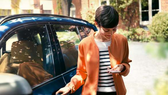 Moteris žiūri į išmanųjį telefoną Iš BMW išlipanti moteris žiūri į išmanųjį telefoną