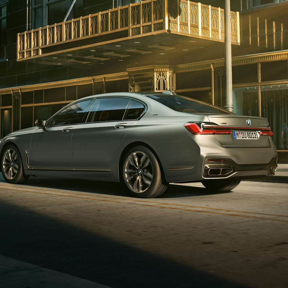 BMW M760Li xDrive su V12 varikliu Vaizdas iš galinio šono į BMW M760Li xDrive, stovintį priešais dangoraižius miesto fone