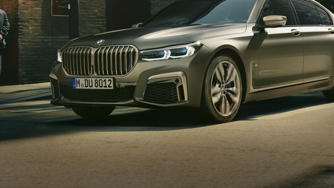 BMW M760Li xDrive miesto fone Vaizdas iš priekinio šono į BMW M760Li xDrive, važiuojantį gatve miesto fone.