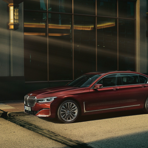 BMW Individual 7 serijos sedanas, šoninis vaizdas Raudono BMW Individual 7 serijos sedano šoninis vaizdas iš priekio miesto fone