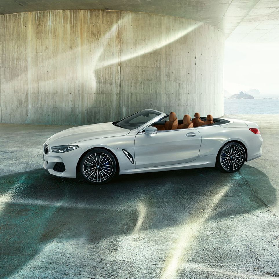 BMW M850i xDrive „Mineral White“ balto metaliko spalvos, vaizdas iš šono su atviru minkštu stogu. BMW M850i xDrive „Mineral White“ balto metaliko spalvos, vaizdas iš šono su atviru minkštu stogu.