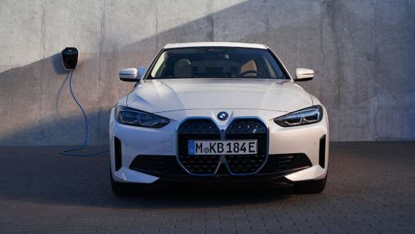 Vaizdas iš priekio prie BMW sieninės įkrovimo stotelės, BMW i4 eDrive40 (G26) 2021 BMW i4 eDrive40 (G26) 2021 baltos Mineral White spalvos, trijų ketvirčių vaizdas iš priekio įkrovimo stotelėje