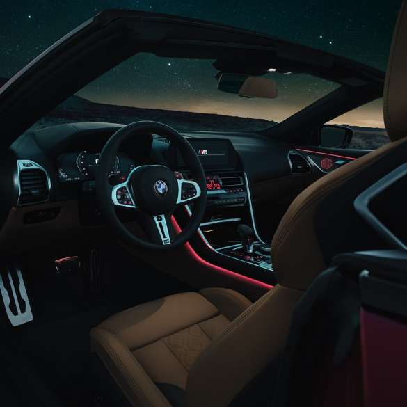 BMW M8 Competition kabrioletas, vairuotojo erdvė. BMW M8 Competition kabrioletas, vairuotojo erdvės su M odiniu vairu ir raudonu apšvietimu vaizdas naktį.