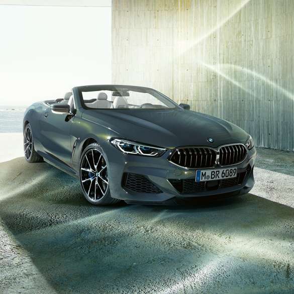 BMW M850i xDrive kabrioletas, trijų ketvirčių vaizdas iš priekio. BMW M850i xDrive kabrioletas Dravit Grey pilko metaliko spalvos su atviru minkštu stogu, trijų ketvirčių pakrantės fone stovinčio automobilio vaizdas iš priekio.