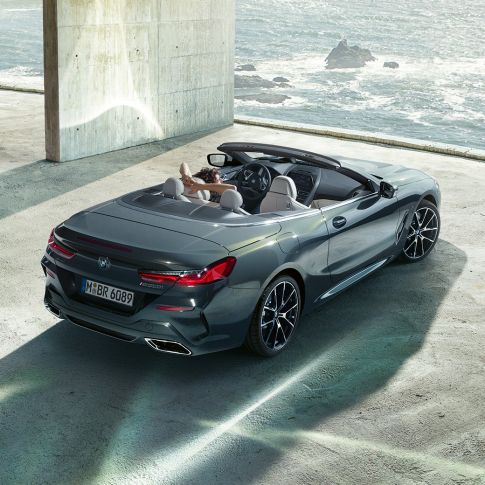 BMW M850i xDrive kabrioletas, vaizdas iš paukščio skrydžio. BMW M850i xDrive kabrioletas Dravit Grey pilko metaliko spalvos su atviru minkštu stogu, vaizdas iš paukščio skrydžio, automobilis parkuojamas pastate vandenyno fone.