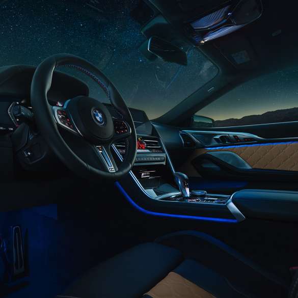 BMW M8 Competition kupė vairuotojo ervdė BMW M8 Competition kupė, vairuotojo erdvės su M odiniu vairu ir mėlynu apšvietimu vaizdas naktį