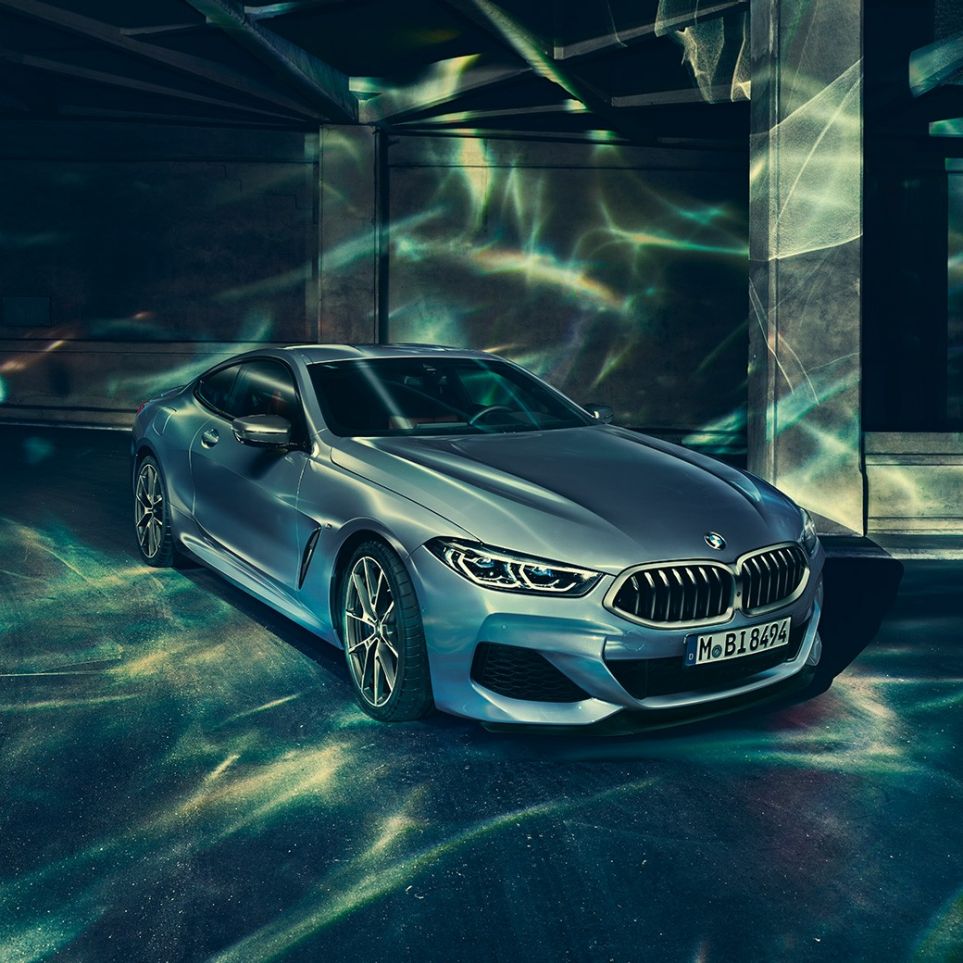 BMW M850i xDrive Coupé, trijų ketvirčių vaizdas iš priekinės dešinės pusės BMW M850i xDrive kupė Barcelona Blue mėlyno metaliko spalvos, trijų ketvirčių priešais pastatą stovinčio automobilio vaizdas iš priekinės dešinės pusės