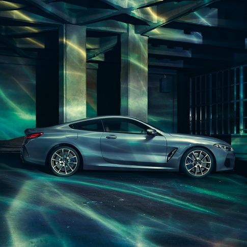 BMW M850i xDrive kupė, vaizdas iš šono BMW M850i xDrive kupė Barcelona Blue mėlyno metaliko spalvos, šoninis prie pastato stovinčio automobilio vaizdas