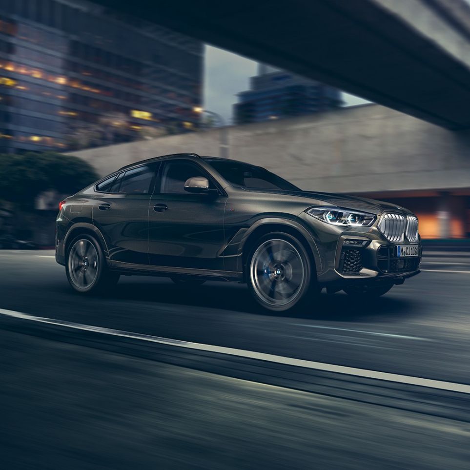Važiuojantis BMW X6 Važiuojančio BMW X6 trijų ketvirčių vaizdas iš priekio miesto fone