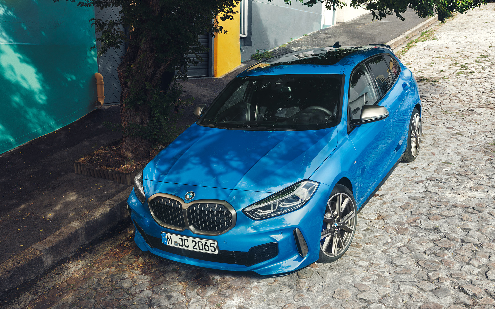 BMW 1 serijos M135i (F40) šalikelėje BMW 1 serijos M135i F40 mėlynos metalizuotos Misano Blue spalvos, šalikelėje parkuojamo automobilio trijų ketvirčių vaizdas iš paukščio skrydžio