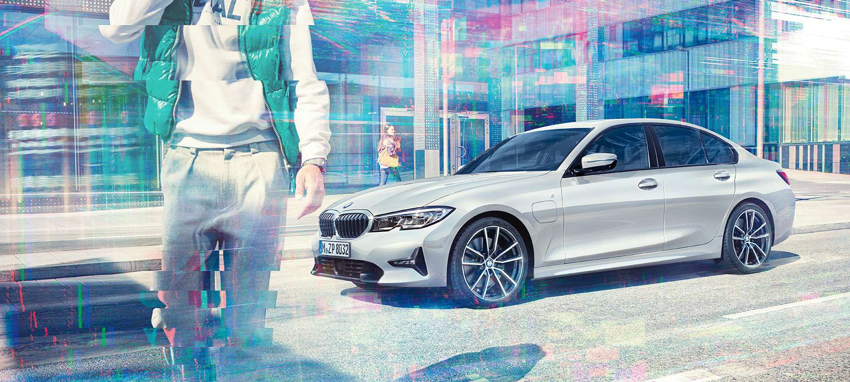 BMW 3 serijos sedanas, BMW 330e vaizdas iš šono Priešais stiklinį miesto pastatą šalia einančių keleivių stovinčio BMW 330e sedano trijų ketvirčių vaizdas iš šono