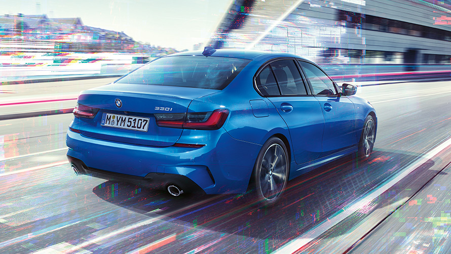 BMW 3 serijos sedano (G20) šoninis vaizdas iš galo Miesto fone dienos metu važiuojančio BMW 3 serijos sedano (G20) trijų ketvirčių vaizdas iš galo