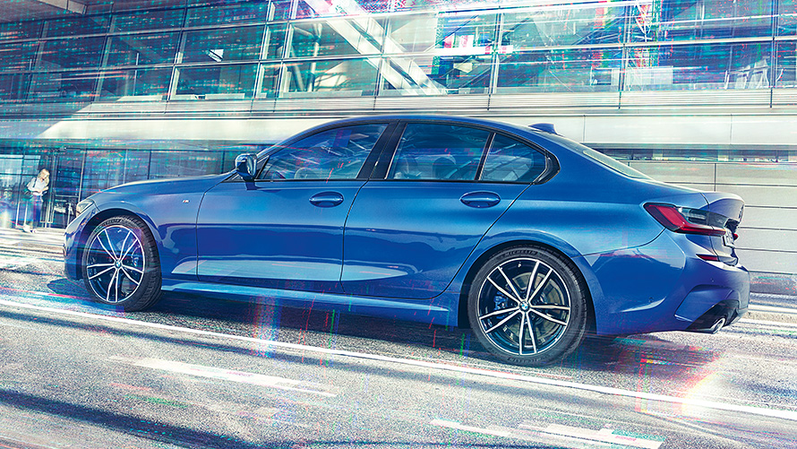 BMW 3 serijos sedanas (G20), dienos metu stovintis priešais stiklinį pastatą Priešais stiklinį pastatą dienos metu stovinčio mėlynos Portimao Blue spalvos 3 serijos BMW sedano (G20) vaizdas iš šono.