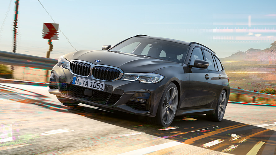 BMW 3 serijos Touring (G21) pilkos <i>Dravite Grey</i> spalvos, trijų ketvirčių vaizdas iš priekio BMW 3 serijos Touring (G21) pilkos <i>Dravite Grey</i> spalvos, užmiesčio fone važiuojančio automobilio trijų ketvirčių vaizdas iš priekio