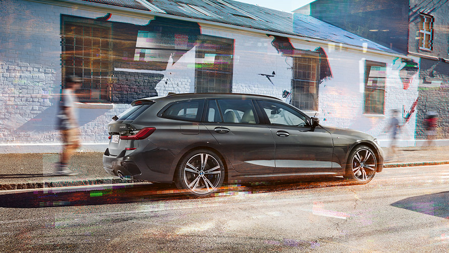 BMW 3 serijosTouring (G21), pilkos <i>Dravit grey</i> spalvos, 7/8 vaizdas iš galo BMW 3 serijosTouring (G21), pilkos <i>Dravit grey</i> spalvos, 7/8 vaizdas iš galo pastato fone