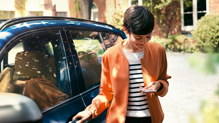 BMW servisas, moteris su išmaniuoju telefonu rankose stovi prie savojo BMW durelių BMW servisas, moteris su išmaniuoju telefonu rankose stovi prie savojo BMW durelių