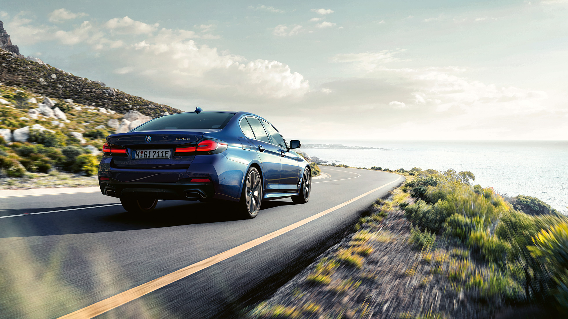 Vairavimo dinamika, BMW 5 serijos sedanas G30 Vairavimo dinamika, BMW 5 serijos sedanas G30 mėlynos Phytonic Blue spalvos, važiuojančio automobilio trijų ketvirčių vaizdas iš galo.