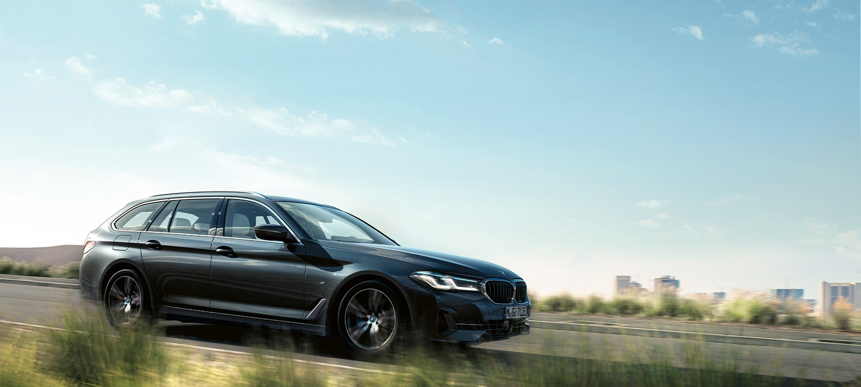 BMW 5 serijos Touring G31 Facelift 2020 pilkos Sophisto Grey spalvos, užmiesčio fone važiuojančio automobilio trijų ketvirčių vaizdas iš priekio