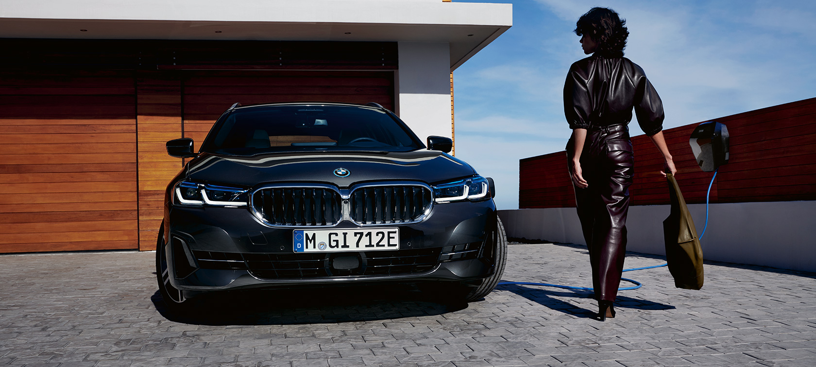 Įkraunamas hibridinis BMW 5 serijos Touring (G31) 2021 LCI, vaizdas iš priekio įkrovimo stotelėje Įkraunamas hibridinis BMW 5 serijos Touring 2021 (G31) LCI, vaizdas iš priekio įkrovimo stotelėje su modeliu
