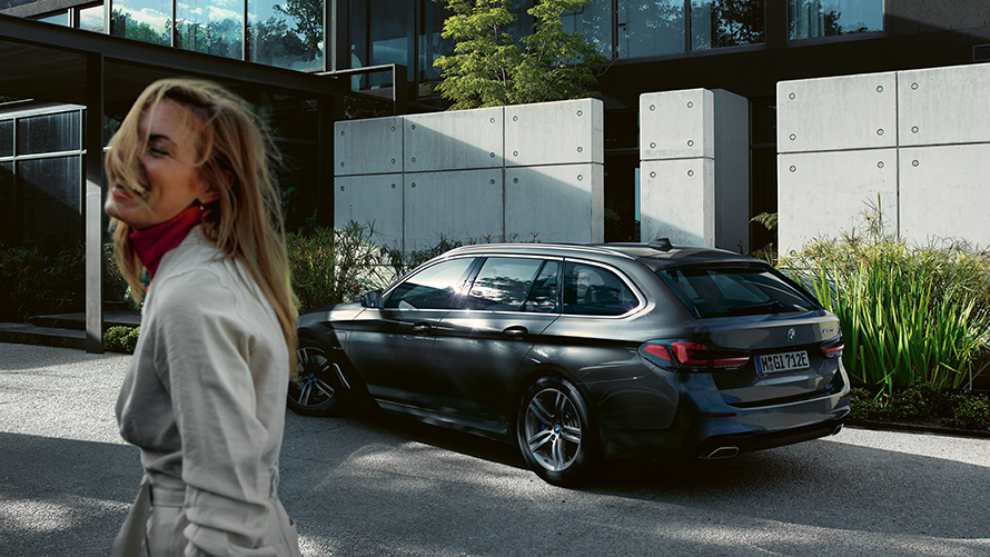 Moteris prie BMW 5 serijos Touring (G31) LCI pilkos metalizuotos Sophisto Grey Brilliant Effect spalvos, 7/8 vaizdas iš šono Moteris parkuoja BMW 5 serijos Touring (G31) Facelift 2020 pilkos metalizuotos Sophisto Grey Brilliant Effect spalvos, 7/8 vaizdas iš šono