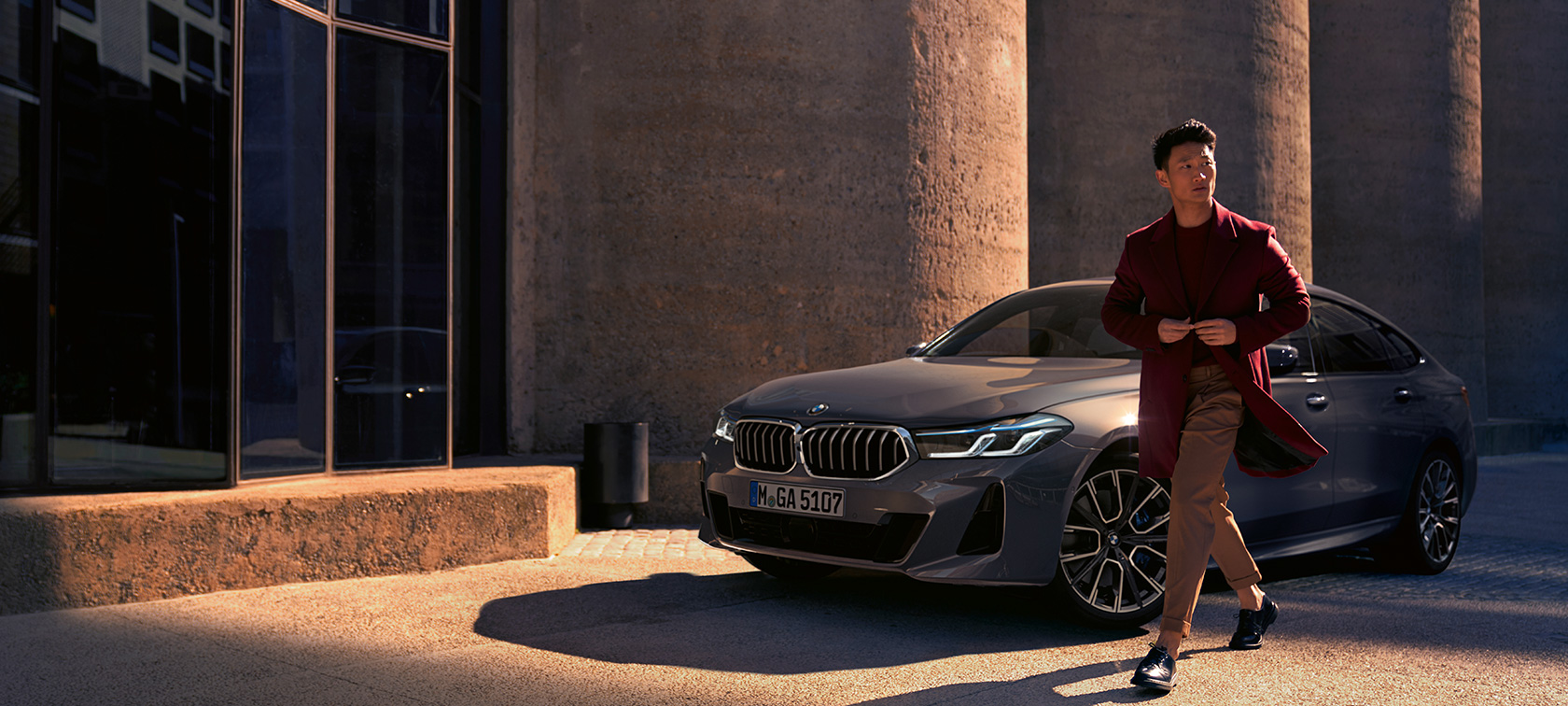 BMW 6 serijos Gran Turismo 640i xDrive G32 2020 pilkos Bernina Grey spalvos, trijų ketvirčių vaizdas iš priekio, šalia BMW stovintis vyras