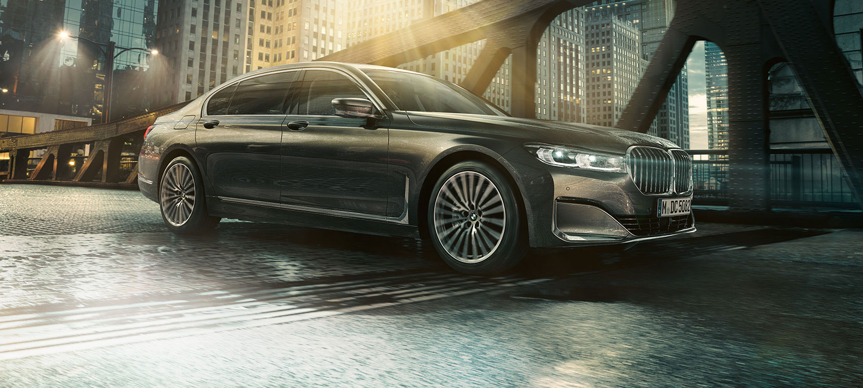 BMW 7 serijos sedano vaizdas iš šono 7 serijos BMW sedanas atidarytomis durelėmis, priešais apšviestą viešbutį.