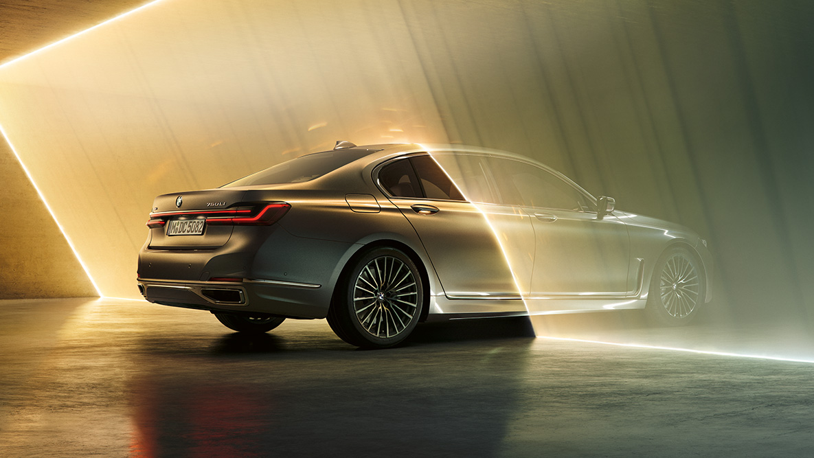 BMW 7 serijos sedanas (G11 G12) 2019 pilkos Bernina Grey spalvos BMW 7 serijos sedanas (G11 G12) 2019 pilkos Bernina Grey spalvos su tviskančio gintaro efektu, šviesos spindulių apšviesto automobilio trijų ketvirčių vaizdas iš galo