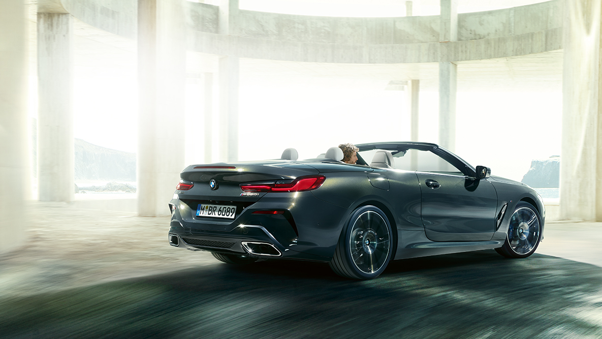 Važiuojantis keliu BMW M850i xDrive su atviru stogu, vaizdas iš šono. Važiuojantis keliu BMW M850i xDrive su atviru stogu, vaizdas iš šono.