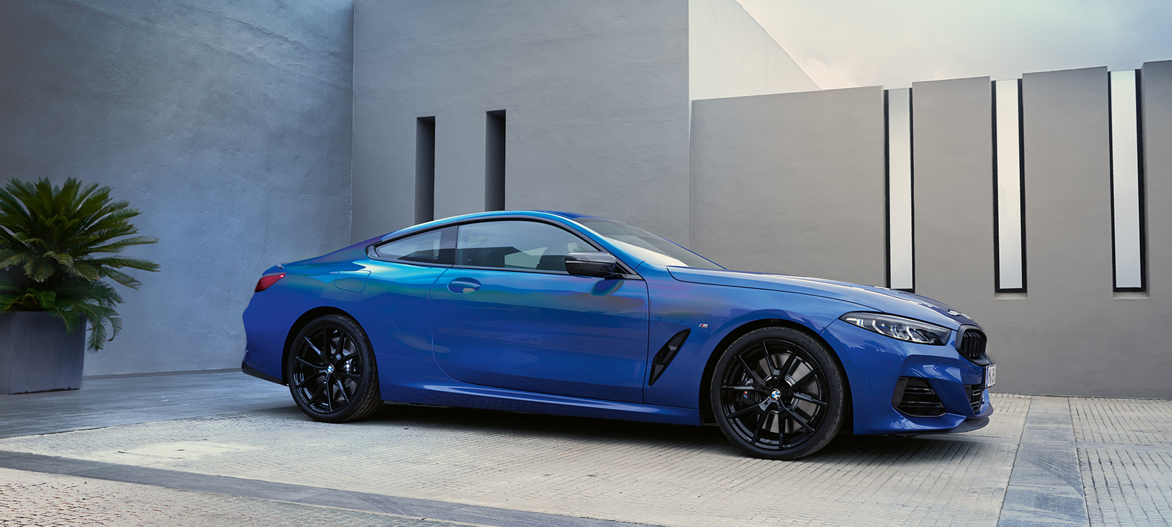 BMW 8 serijos kupė G15 LCI 𝘍𝘢𝘤𝘦𝘭𝘪𝘧𝘵 2022 metalizuotos mėlynos 𝘔 𝘗𝘰𝘳𝘵𝘪𝘮𝘢𝘰 𝘉𝘭𝘶𝘦 kėbulo spalvos namo sienos fone stovinčio automobilio vaizdas iš priekio