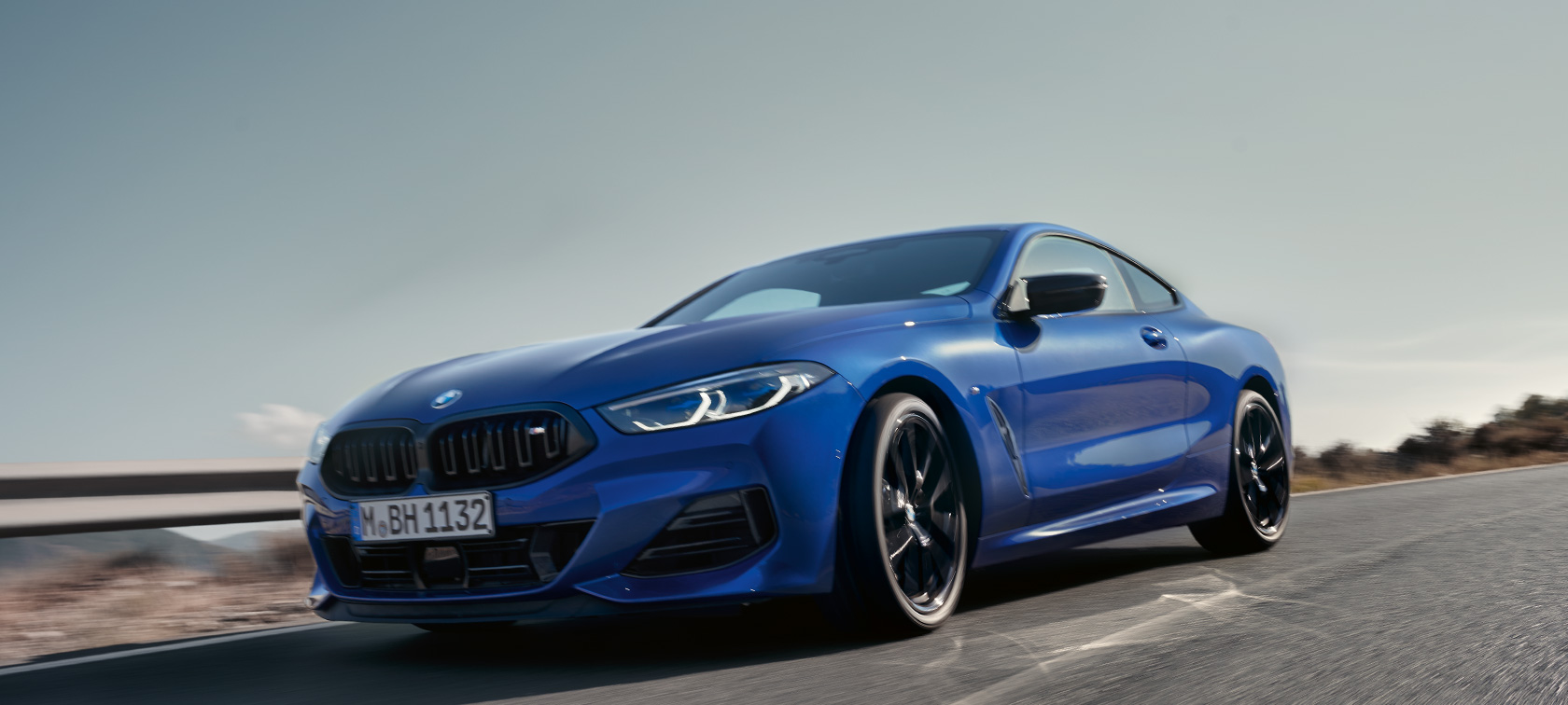 BMW 8 serijos kupė G15 LCI Facelift 2022 BMW M850i xDrive M Portimao Blue mėlynos metalizuotos spalvos užmiesčio keliu kalvų fone važiuojančio automobilio vaizdas iš priekio žemu kampu BMW 8 serijos kupė G15 LCI Facelift 2022 BMW M850i xDrive M Portimao Blue mėlynos metalizuotos spalvos užmiesčio keliu kalvų fone važiuojančio automobilio vaizdas iš priekio žemu kampu