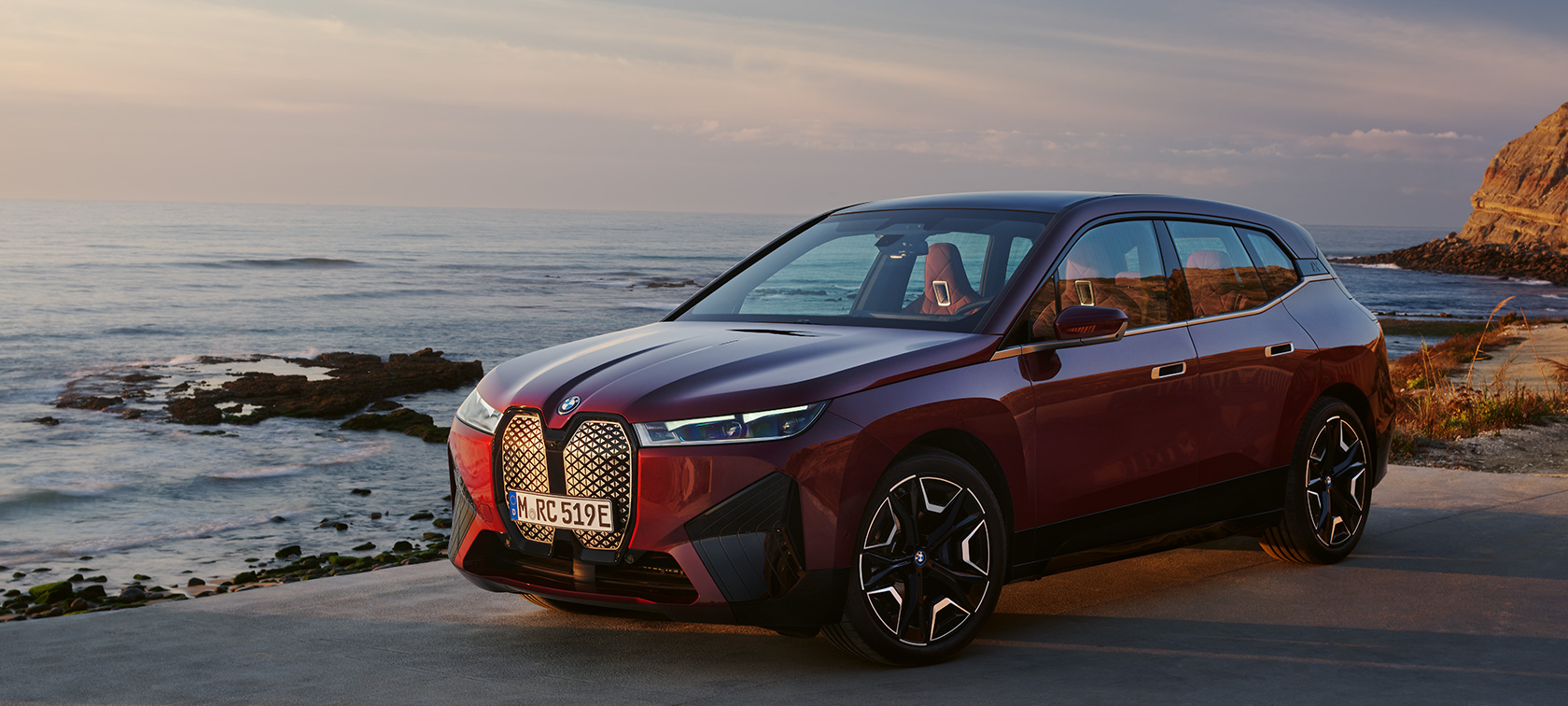 BMW iX i20 2021 elektrinis SUV BMW iX xDrive50 Aventurin Red raudonos spalvos pakrantės fone