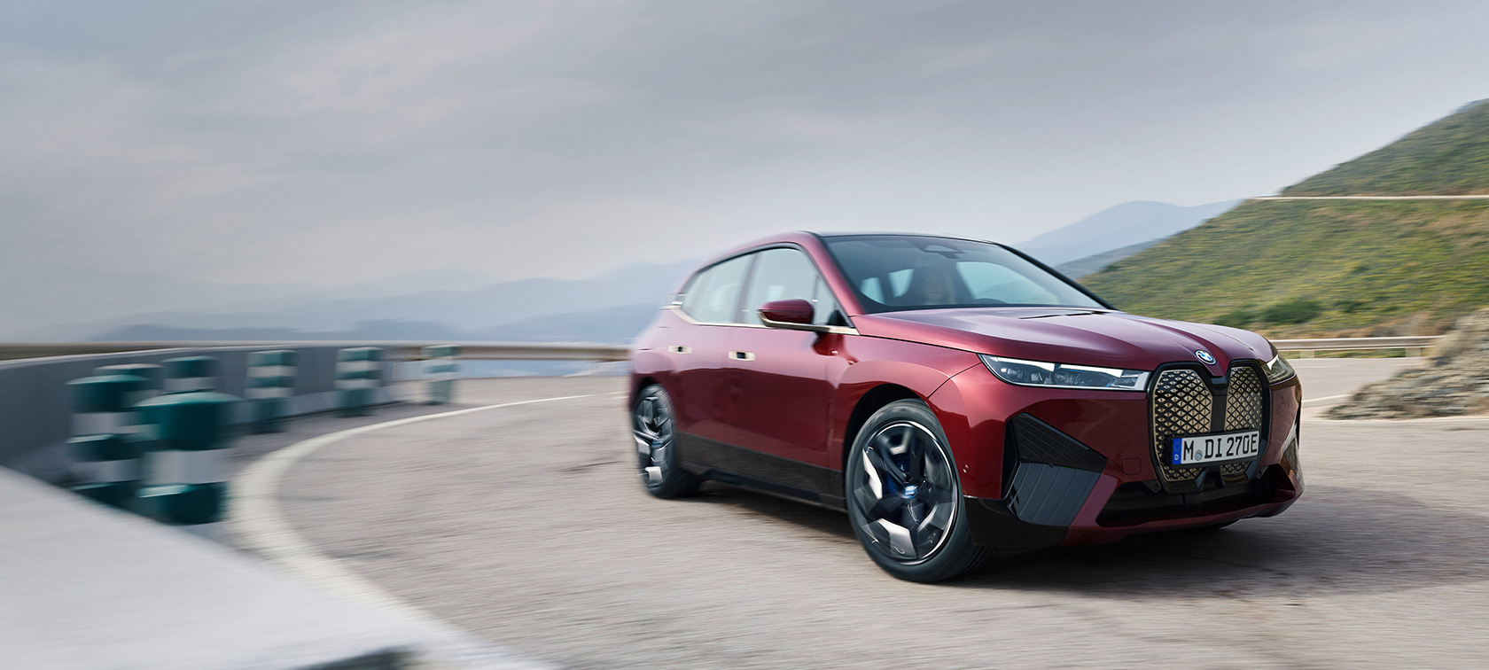BMW iX (i20) 2021 elektrinis SUV BMW iX xDrive50 raudonos Aventurin Red spalvos pakrantės fone