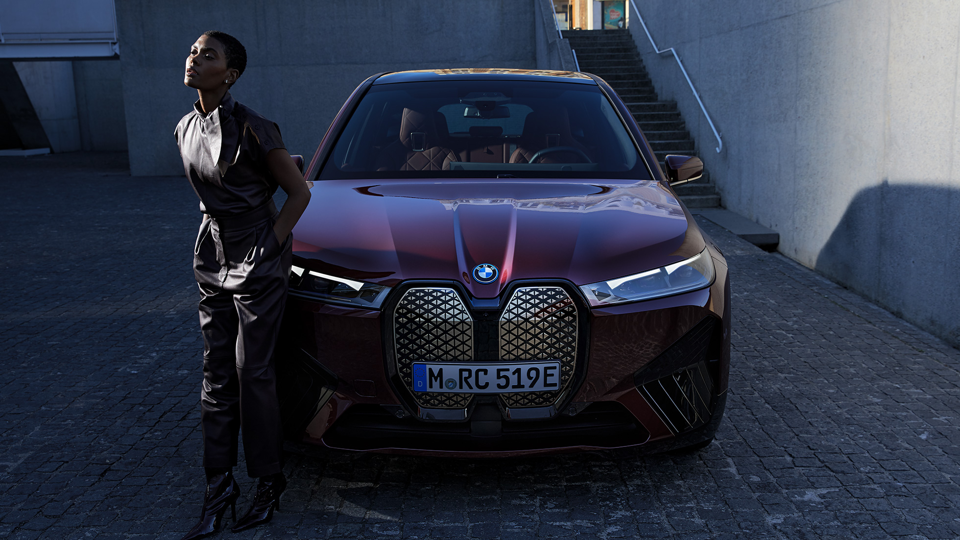 BMW iX vaizdas iš priekio su modeliu BMW iX raudonos Aventurin Red spalvos i20 vaizdas iš priekio su modeliu