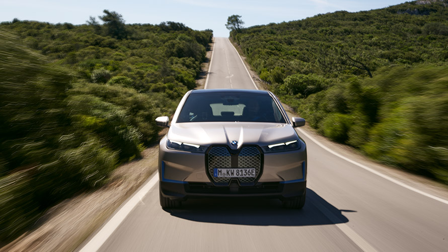 BMW iX keliu važiuojančio automobilio vaizdas iš priekio BMW iX sidabro Cashmere Silver spalvos i20 keliu važiuojančio automobilio vaizdas iš priekio