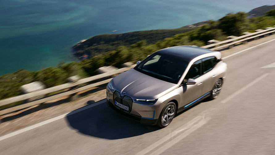BMW iX keliu važiuojančio automobilio vaizdas iš paukščio skrydžio BMW iX sidabro Cashmere Silver spalvos i20 keliu važiuojančio automobilio vaizdas iš paukščio skrydžio