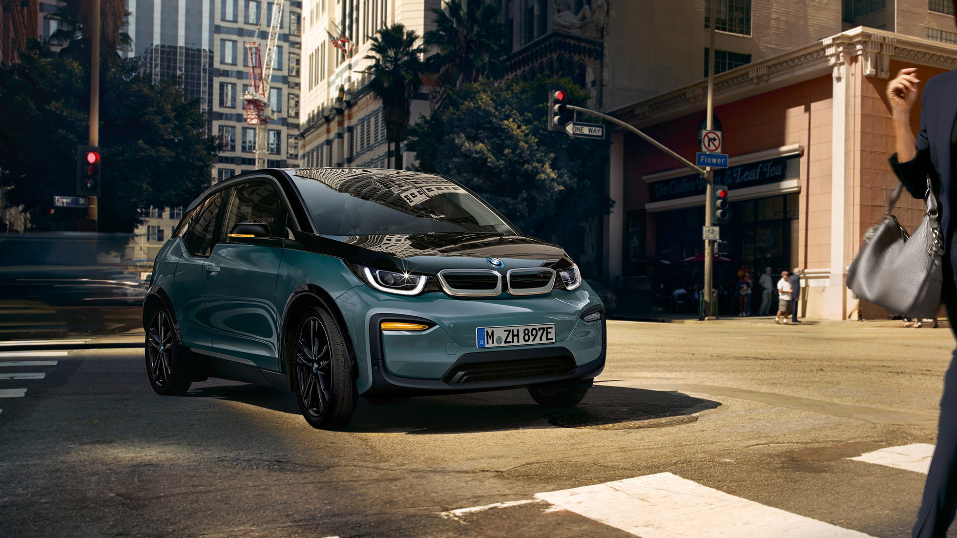 BMW i3 2018 trijų ketvirčių važiuojančio automobilio vaizdas iš priekio BMW i3 I01 2018 Jucaro beige smėlio spalvos su Frozen Grey pilko metaliko spalvos akcentu, trijų ketvirčių važiuojančio automobilio vaizdas iš priekio miesto fone