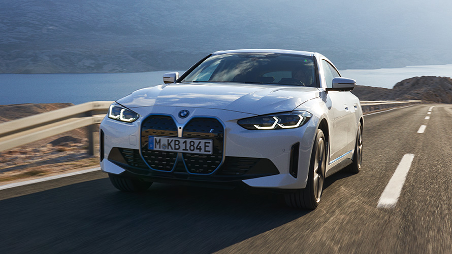 Trijų ketvirčių vaizdas iš priekio, keliu važiuojantis BMW i4 eDrive40 (G26) 2021 BMW i4 eDrive40 (G26) 2021, važiuojančio automobilio baltos Mineral White spalvos, trijų ketvirčių vaizdas iš priekio
