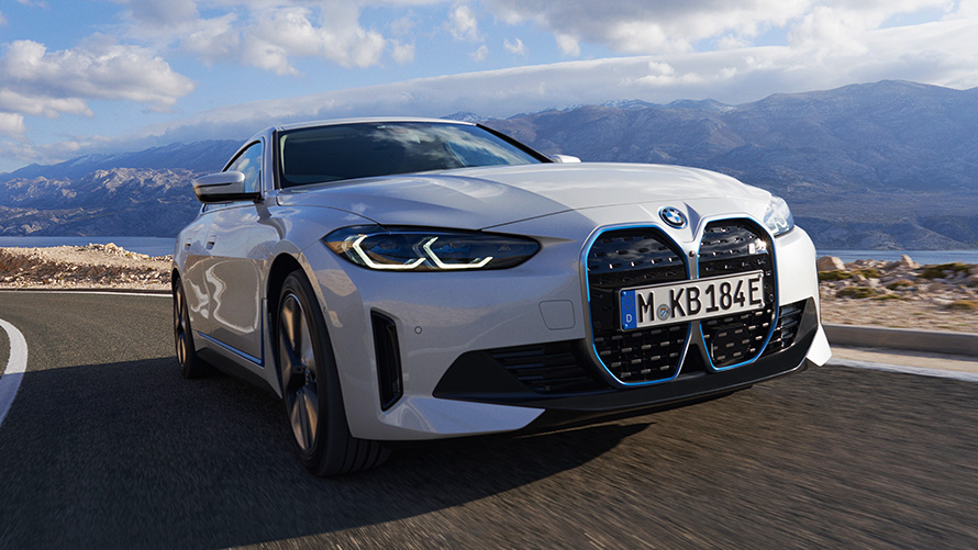 Trijų ketvirčių vaizdas iš priekio, keliu važiuojantis BMW i4 eDrive40 (G26) 2021 BMW i4 eDrive40 (G26) 2021 baltos Mineral White spalvos, važiuojančio automobilio trijų ketvirčių vaizdas iš priekio