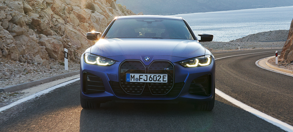 Važiuojančio BMW i4 M50 (G26) 2021 vaizdas iš priekio BMW i4 M50 (G26) 2021 M mėlynos metalizuotos Portimao Blue kėbulo spalvos, keliu važiuojančio automobilio vaizdas iš priekio