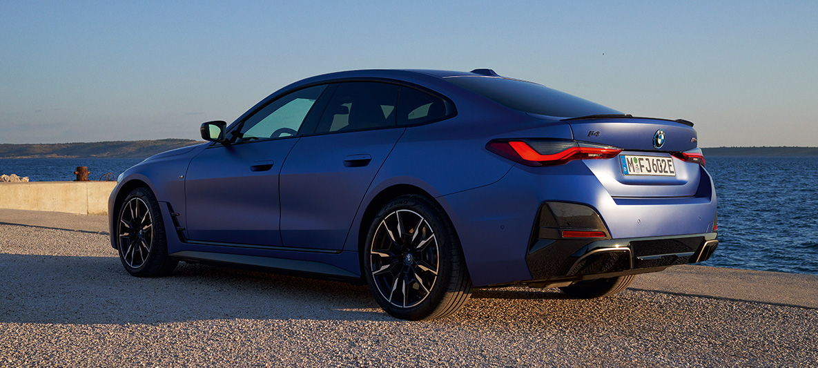 Trijų ketvirčių vaizdas iš galo, BMW i4 M50 (G26) 2021 BMW i4 M50 (G26) 2021 M mėlynos metalizuotos Portimao Blue kėbulo spalvos, trijų ketvirčių vaizdas iš galo prieplaukos fone